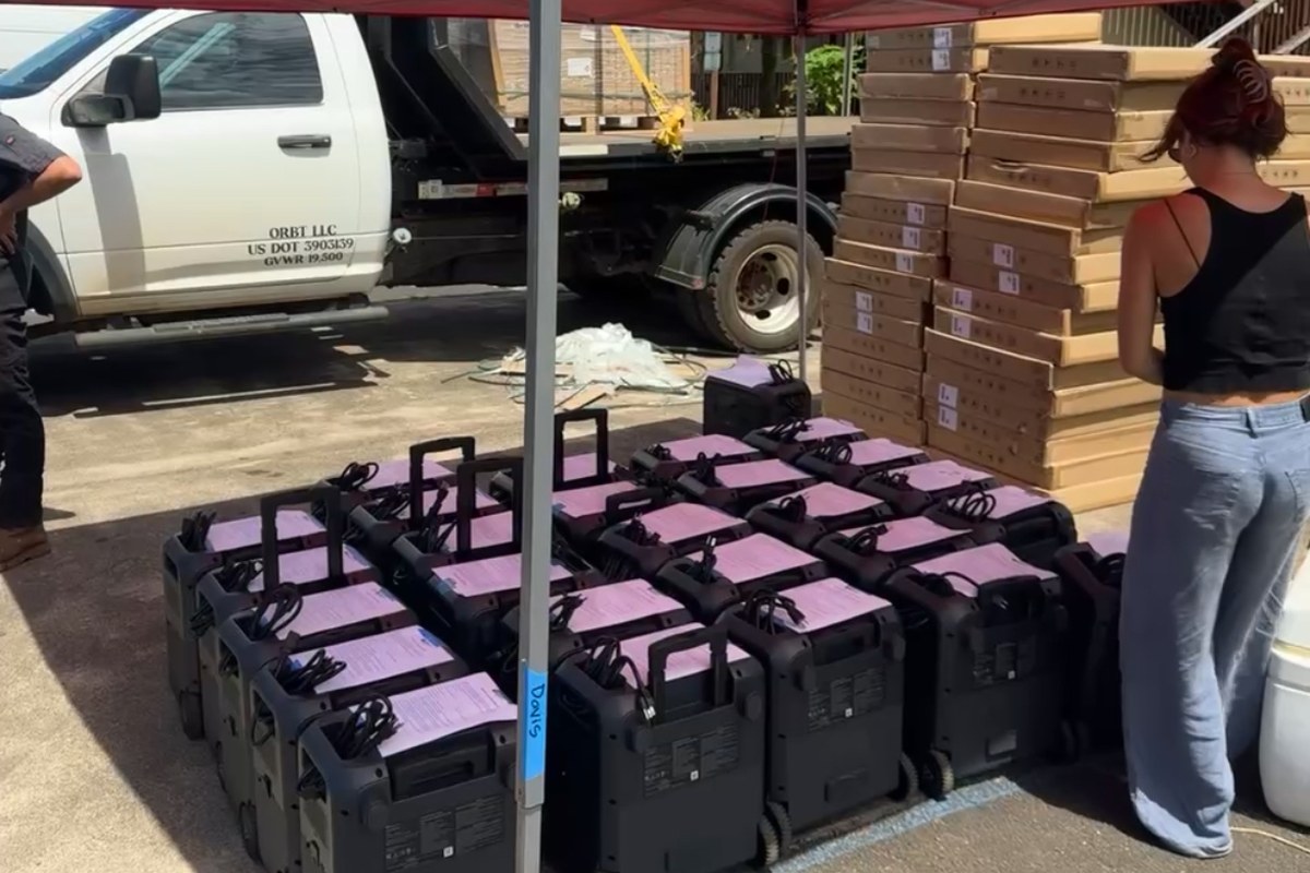 Rows of BLUETTI portable power stations staged under a tent with solar panel boxes stacked behind them